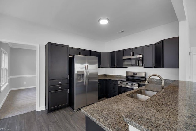 kitchen with kitchen peninsula, stainless steel appliances, dark stone counters, and sink