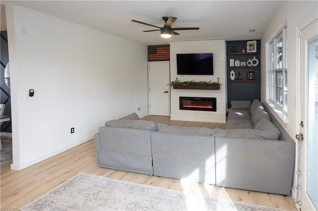 living room featuring a large fireplace, light hardwood / wood-style floors, ceiling fan, and a healthy amount of sunlight