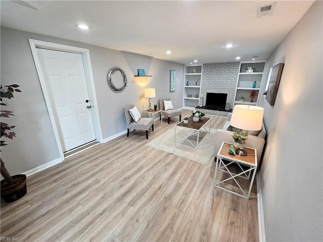 living room featuring a fireplace, built in shelves, and light hardwood / wood-style flooring