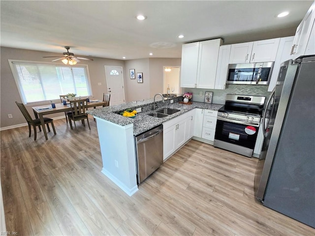 kitchen with kitchen peninsula, appliances with stainless steel finishes, light stone countertops, sink, and white cabinetry