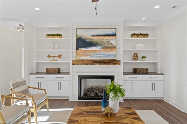 interior space featuring a large fireplace, built in features, ornamental molding, and dark wood-type flooring