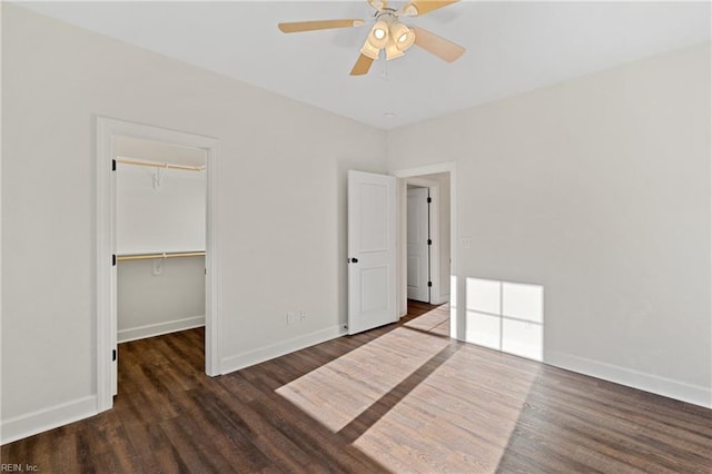 unfurnished bedroom featuring a walk in closet, a closet, ceiling fan, and dark wood-type flooring