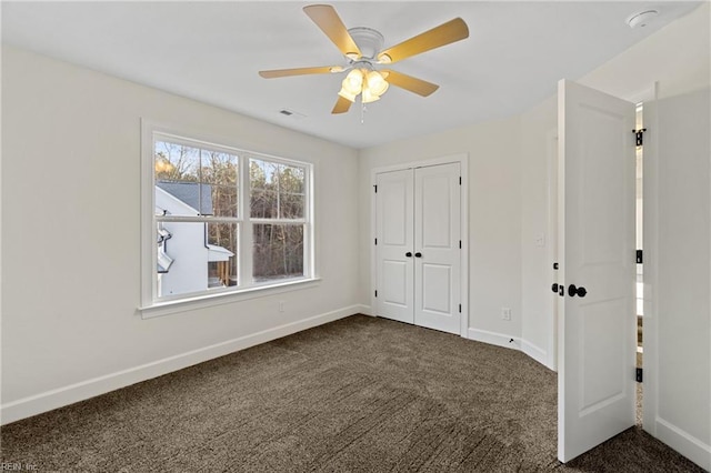 unfurnished bedroom with dark colored carpet, ceiling fan, and a closet