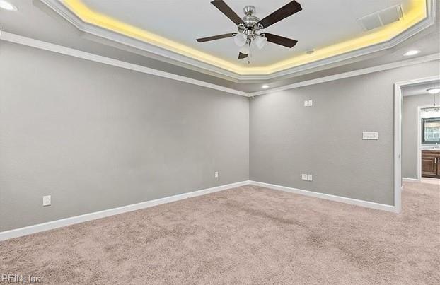 carpeted empty room featuring a raised ceiling, ceiling fan, and ornamental molding