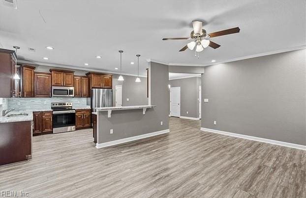 kitchen featuring backsplash, decorative light fixtures, a kitchen bar, appliances with stainless steel finishes, and ornamental molding