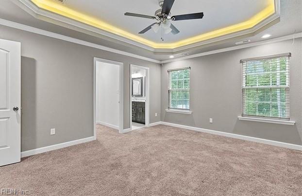 unfurnished bedroom with ensuite bath, ceiling fan, a raised ceiling, light carpet, and ornamental molding