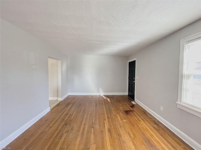 empty room with hardwood / wood-style floors, a textured ceiling, and plenty of natural light