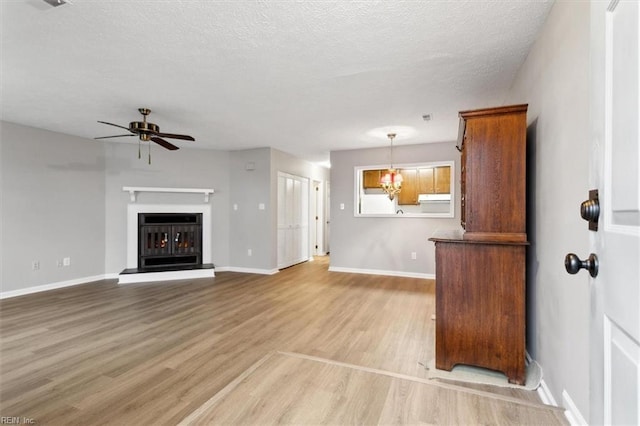 unfurnished living room featuring a textured ceiling, ceiling fan with notable chandelier, and light wood-type flooring