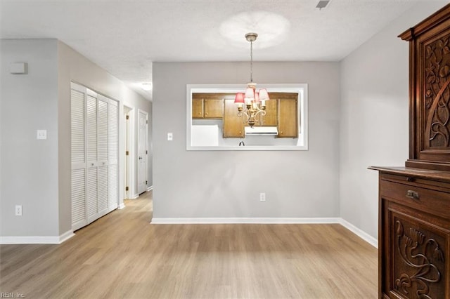 unfurnished dining area featuring an inviting chandelier and light hardwood / wood-style flooring