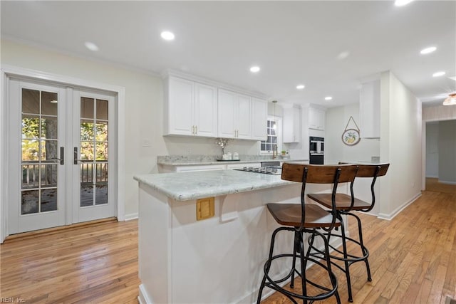 kitchen featuring a kitchen bar, french doors, light stone countertops, light hardwood / wood-style flooring, and white cabinets