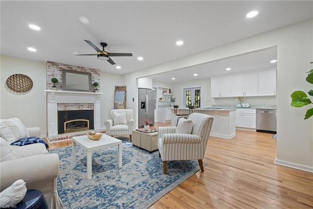 living room featuring ceiling fan, light wood-type flooring, and a brick fireplace