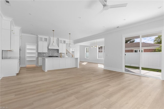 unfurnished living room featuring ceiling fan with notable chandelier, light wood-type flooring, and crown molding