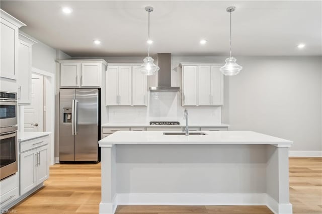 kitchen with wall chimney exhaust hood, stainless steel appliances, decorative light fixtures, a center island with sink, and white cabinets