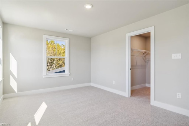 unfurnished bedroom with a spacious closet, a closet, and light carpet