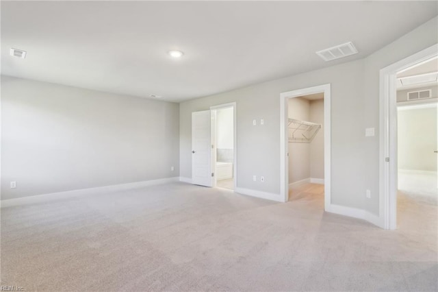 unfurnished bedroom featuring a walk in closet, ensuite bathroom, a closet, and light colored carpet