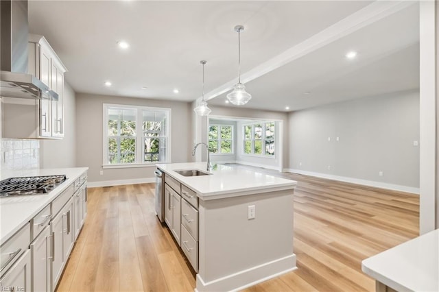 kitchen featuring hanging light fixtures, sink, wall chimney exhaust hood, an island with sink, and appliances with stainless steel finishes