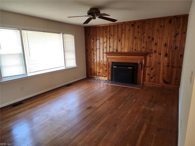 unfurnished living room with ceiling fan, dark hardwood / wood-style flooring, and wooden walls