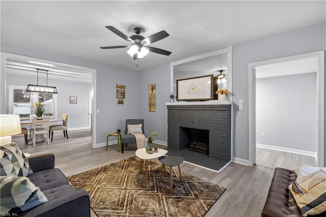 living room with ceiling fan, light wood-type flooring, and a brick fireplace