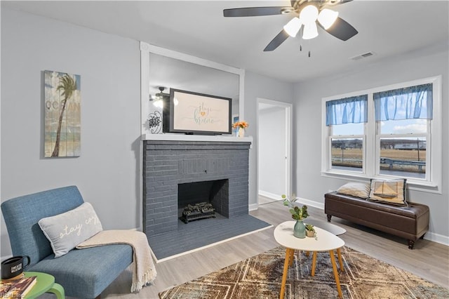 living room with ceiling fan, light hardwood / wood-style flooring, and a brick fireplace