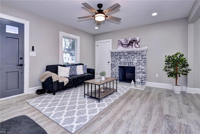 living room with ceiling fan, a fireplace, and light hardwood / wood-style floors