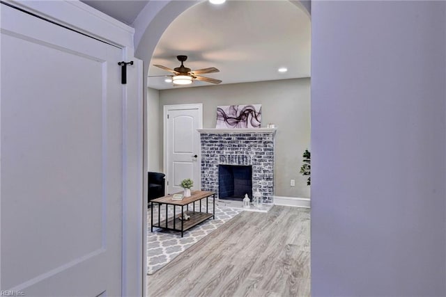 living room featuring ceiling fan, light wood-type flooring, and a brick fireplace