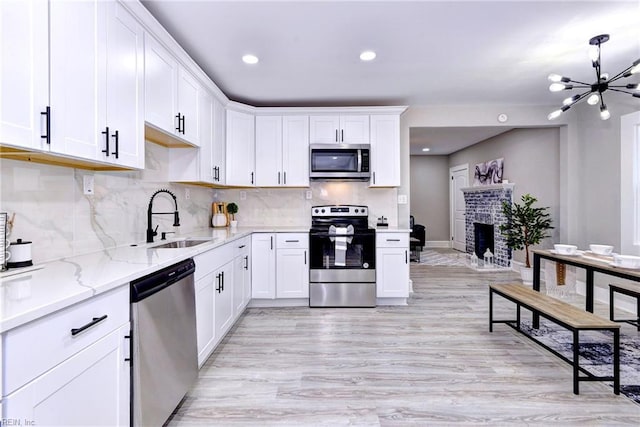 kitchen featuring sink, a brick fireplace, light stone countertops, appliances with stainless steel finishes, and white cabinetry