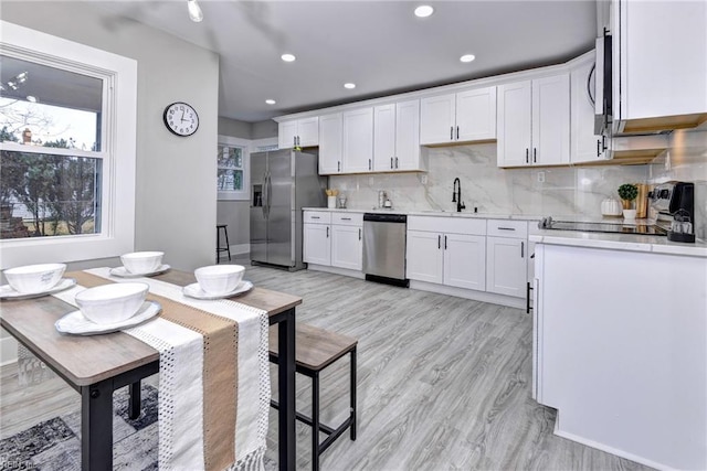 kitchen with light wood-type flooring, tasteful backsplash, stainless steel appliances, sink, and white cabinetry