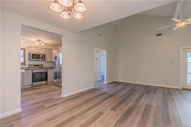 unfurnished living room with ceiling fan with notable chandelier, light hardwood / wood-style floors, and high vaulted ceiling