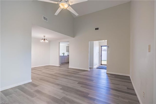 empty room featuring a high ceiling, ceiling fan with notable chandelier, and hardwood / wood-style flooring