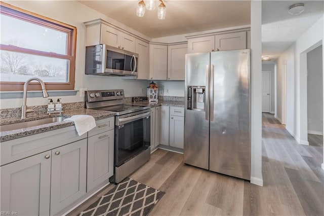 kitchen featuring sink, light hardwood / wood-style floors, stone countertops, and appliances with stainless steel finishes