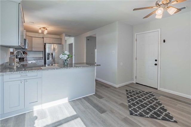 kitchen with kitchen peninsula, stainless steel fridge with ice dispenser, sink, and light stone counters