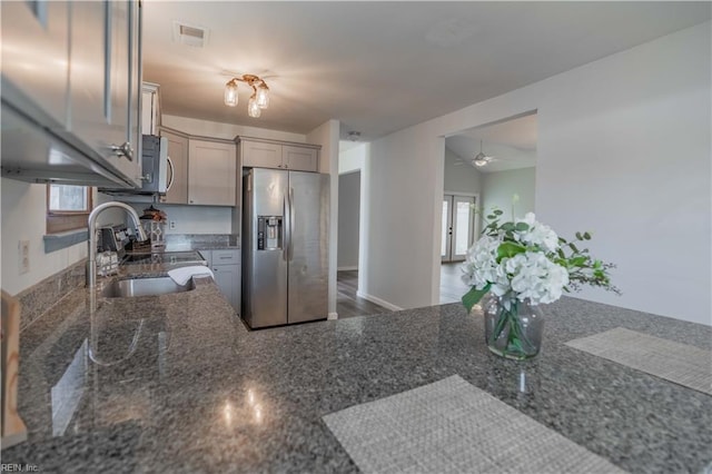 kitchen with gray cabinetry, stainless steel fridge, dark stone countertops, and sink