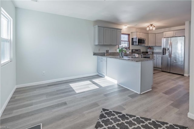 kitchen featuring kitchen peninsula, light wood-type flooring, stainless steel appliances, and dark stone countertops