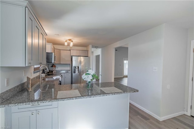 kitchen with kitchen peninsula, light wood-type flooring, stone countertops, and appliances with stainless steel finishes