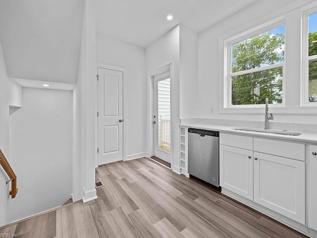 kitchen with stainless steel dishwasher, white cabinets, light wood-type flooring, and sink