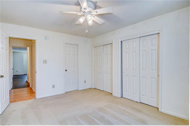 unfurnished bedroom with light colored carpet, ceiling fan, and multiple closets