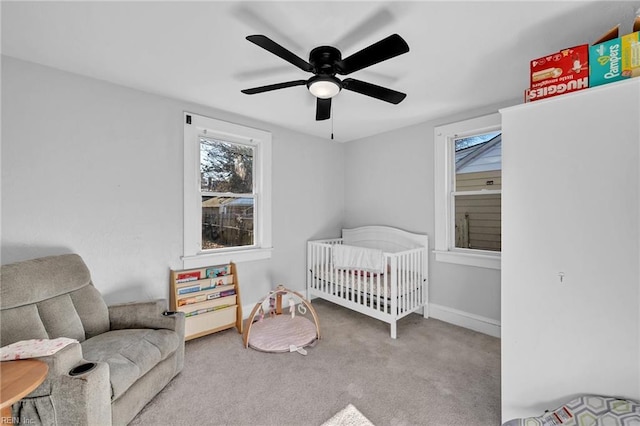 carpeted bedroom featuring ceiling fan and a crib