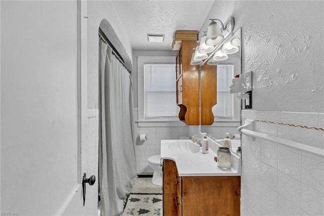 bathroom with vanity, toilet, a textured ceiling, and tile walls