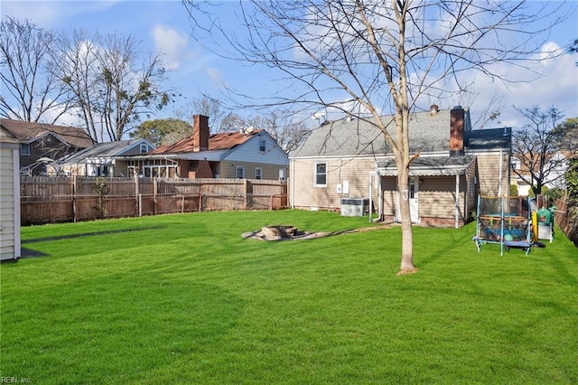 rear view of property with a lawn, central AC unit, and a trampoline