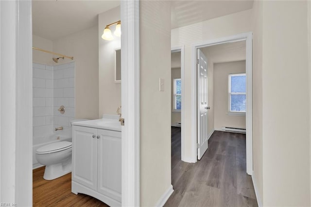 full bathroom with hardwood / wood-style floors, vanity, a baseboard heating unit, shower / washtub combination, and toilet