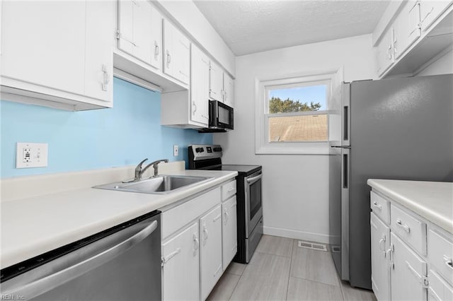 kitchen with appliances with stainless steel finishes, a textured ceiling, white cabinetry, and sink