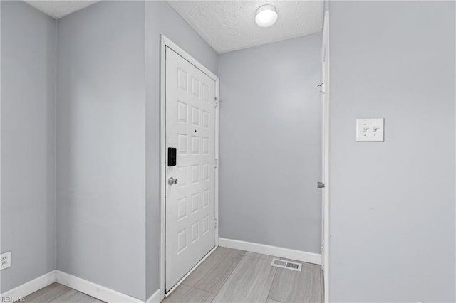 corridor with a textured ceiling and light hardwood / wood-style flooring