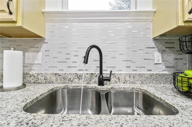 interior details featuring decorative backsplash, sink, light stone counters, and cream cabinetry