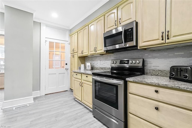 kitchen with appliances with stainless steel finishes, tasteful backsplash, light stone counters, crown molding, and light hardwood / wood-style flooring