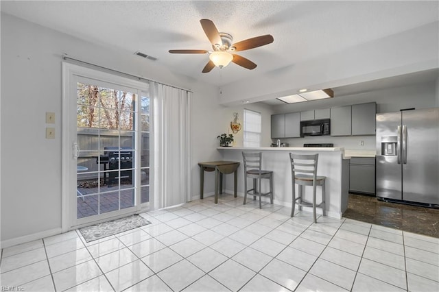 kitchen featuring gray cabinetry, ceiling fan, kitchen peninsula, stainless steel fridge, and a breakfast bar area