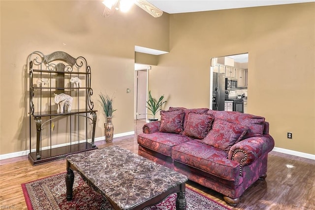 living room featuring hardwood / wood-style floors, ceiling fan, and a towering ceiling