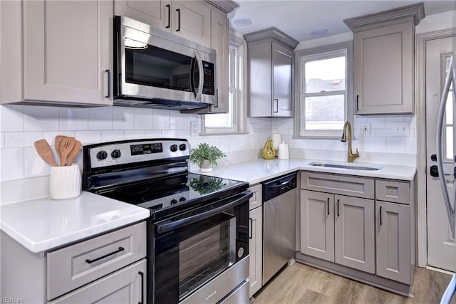 kitchen featuring decorative backsplash, appliances with stainless steel finishes, gray cabinetry, sink, and light hardwood / wood-style flooring