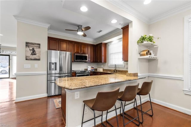 kitchen with kitchen peninsula, appliances with stainless steel finishes, a kitchen breakfast bar, ornamental molding, and sink