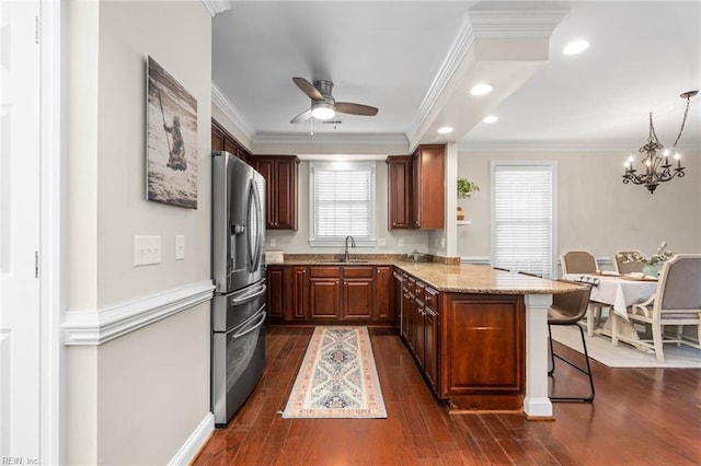 kitchen featuring kitchen peninsula, stainless steel refrigerator with ice dispenser, light stone countertops, a breakfast bar, and decorative light fixtures