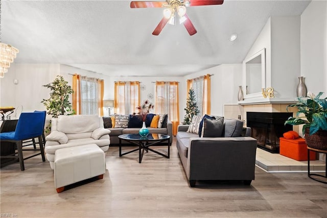 living room featuring ceiling fan, light wood-type flooring, a fireplace, and vaulted ceiling